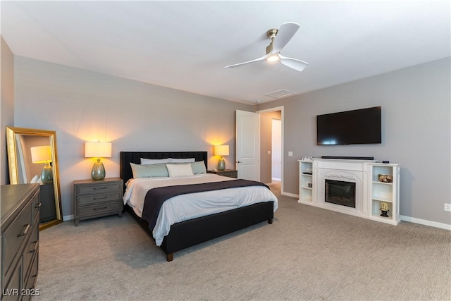 bedroom with ceiling fan, light colored carpet, visible vents, baseboards, and a glass covered fireplace