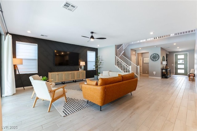 living area with light wood-style floors, an accent wall, stairway, and visible vents