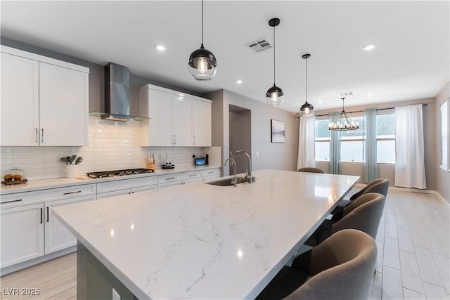 kitchen with visible vents, stainless steel gas stovetop, backsplash, a sink, and wall chimney exhaust hood