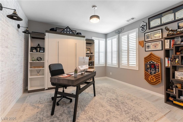 office space featuring visible vents, brick wall, light wood-style flooring, and baseboards