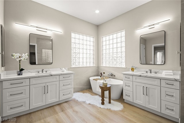 full bath featuring a sink, a freestanding tub, two vanities, and wood finished floors