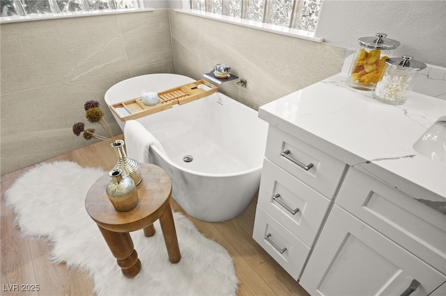 full bathroom with tile walls, a soaking tub, vanity, and wood finished floors