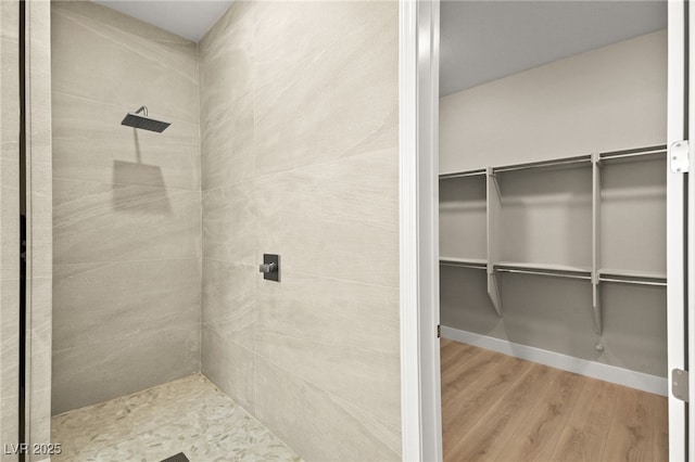 bathroom featuring a walk in closet, tiled shower, and wood finished floors