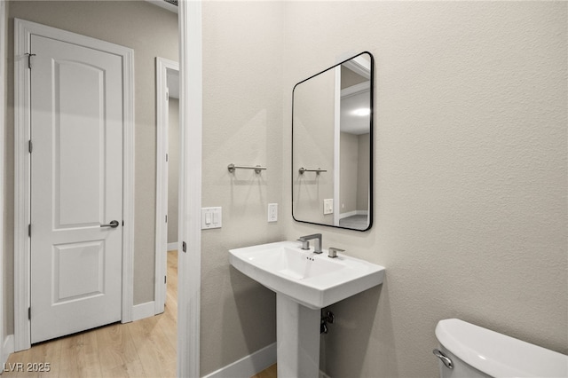 half bathroom with wood finished floors, toilet, and baseboards