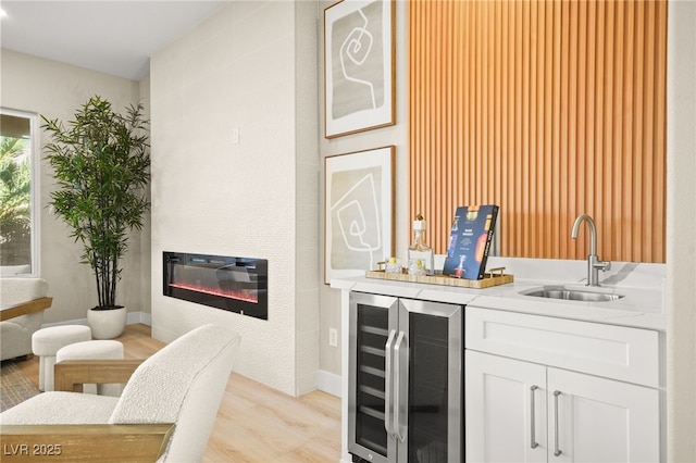 bar featuring wine cooler, light wood finished floors, a large fireplace, a sink, and baseboards