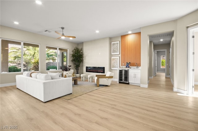 living area with wine cooler, recessed lighting, a large fireplace, light wood-type flooring, and baseboards