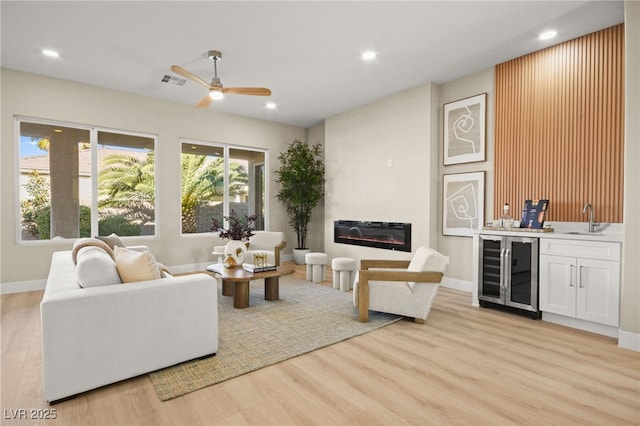 living area featuring visible vents, a glass covered fireplace, wine cooler, wet bar, and light wood-style floors