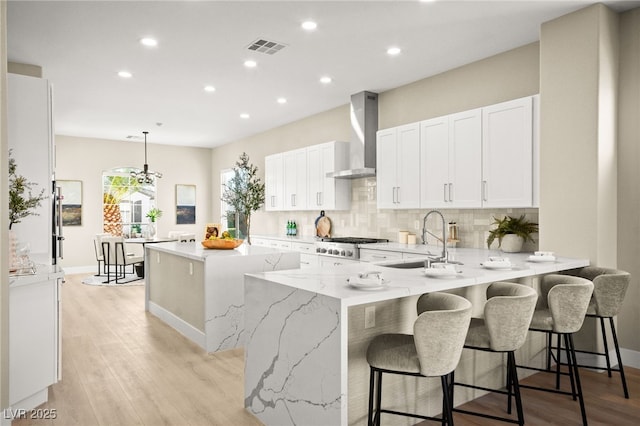 kitchen with a peninsula, a sink, visible vents, backsplash, and wall chimney exhaust hood