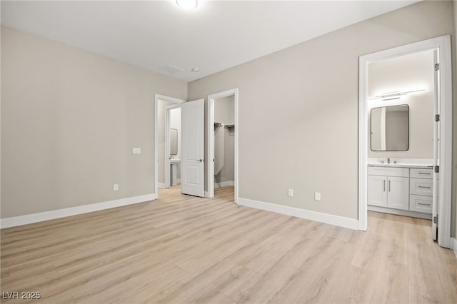 unfurnished bedroom featuring a walk in closet, light wood finished floors, a closet, connected bathroom, and baseboards