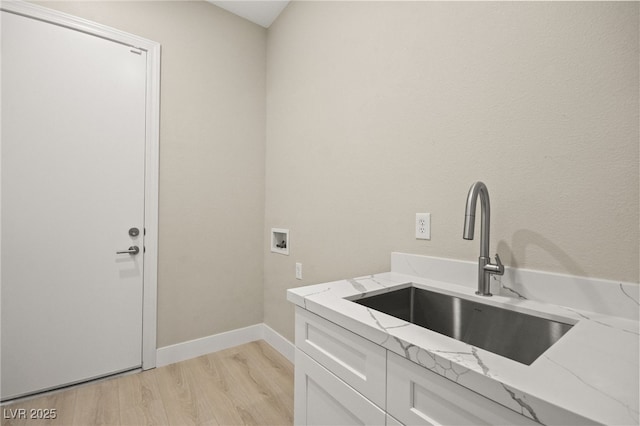 clothes washing area with hookup for a washing machine, a sink, baseboards, light wood-style floors, and cabinet space