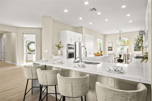 kitchen featuring visible vents, white cabinets, a sink, and a kitchen breakfast bar