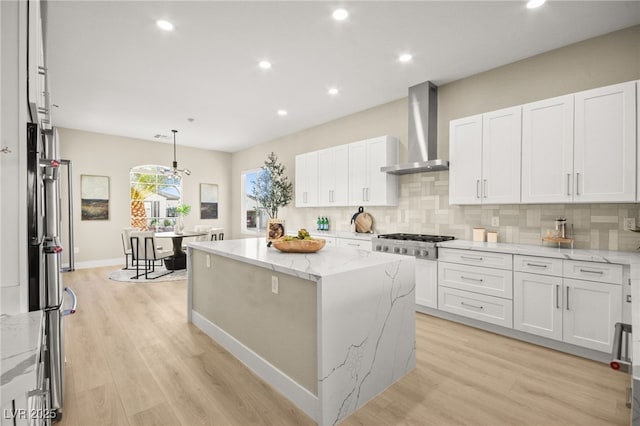 kitchen featuring wall chimney exhaust hood, tasteful backsplash, a kitchen island, and white cabinetry