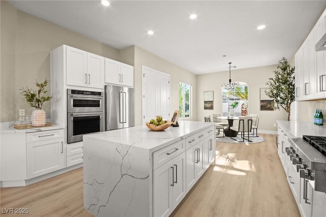 kitchen with light stone counters, a center island, light wood finished floors, stainless steel appliances, and white cabinetry