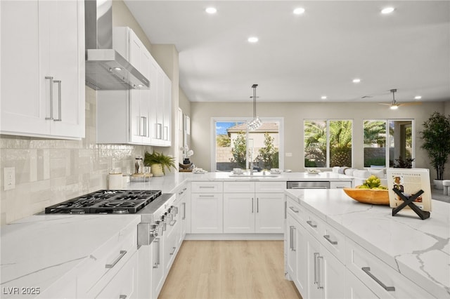 kitchen with light stone counters, wall chimney range hood, appliances with stainless steel finishes, and white cabinets