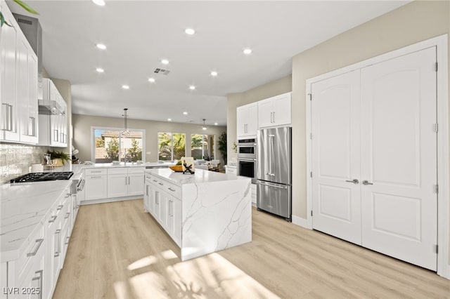 kitchen featuring stainless steel appliances, a kitchen island, light wood-style floors, decorative backsplash, and light stone countertops