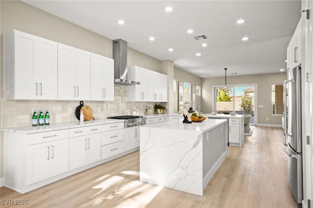 kitchen featuring visible vents, appliances with stainless steel finishes, a center island, wall chimney range hood, and white cabinetry