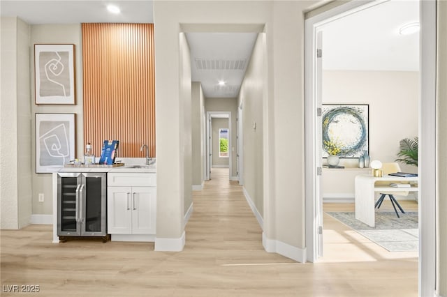 corridor featuring baseboards, visible vents, wine cooler, light wood-style floors, and a sink