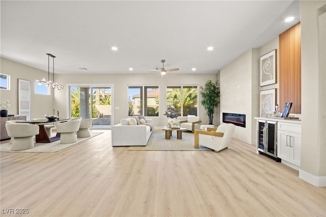 living room featuring wine cooler, recessed lighting, ceiling fan with notable chandelier, a fireplace, and light wood finished floors