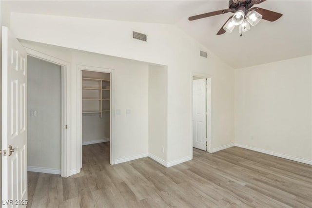 unfurnished bedroom with light wood finished floors, vaulted ceiling, visible vents, and a walk in closet