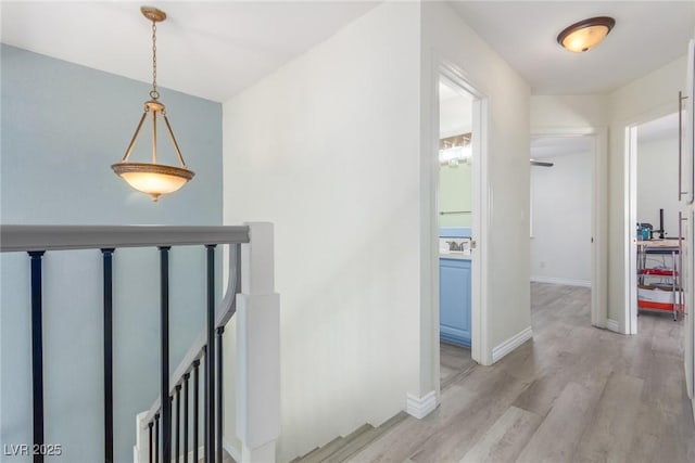 corridor with baseboards, an upstairs landing, and light wood-style floors