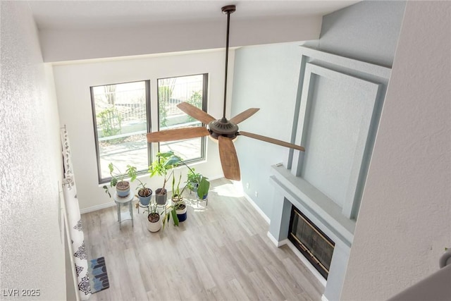 details with visible vents, a ceiling fan, a glass covered fireplace, wood finished floors, and baseboards