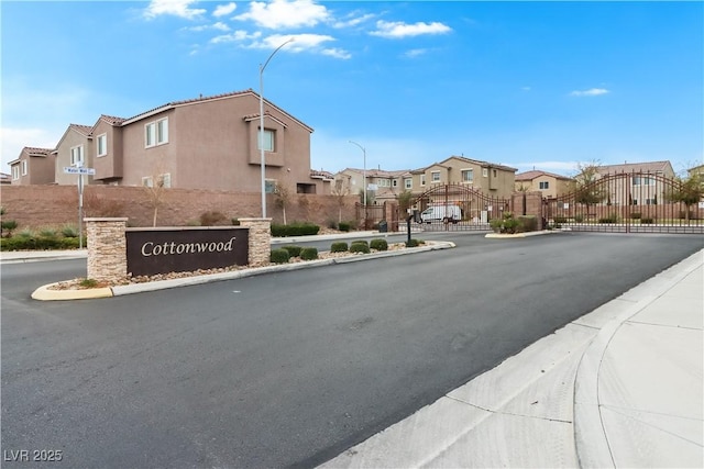 view of road featuring street lights, a gated entry, curbs, a gate, and a residential view