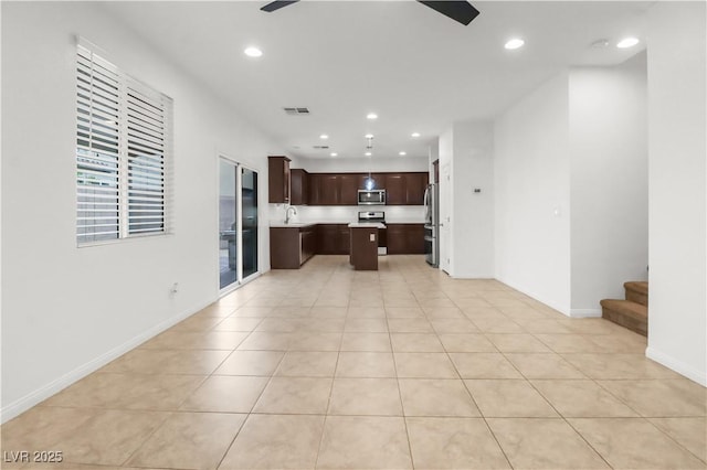 kitchen with a center island, stainless steel appliances, light countertops, open floor plan, and dark brown cabinets