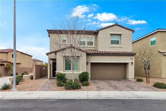 mediterranean / spanish-style house with decorative driveway, stucco siding, an attached garage, fence, and a tiled roof