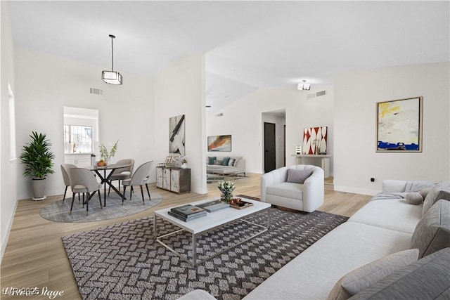 living room with lofted ceiling, light wood-style floors, and visible vents