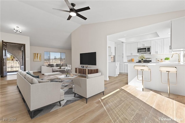 living area featuring vaulted ceiling, ceiling fan, and light wood-style floors