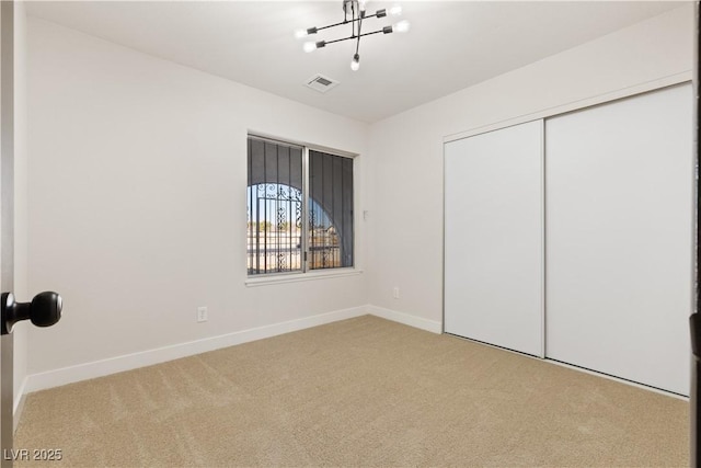 unfurnished bedroom featuring baseboards, visible vents, carpet flooring, a chandelier, and a closet