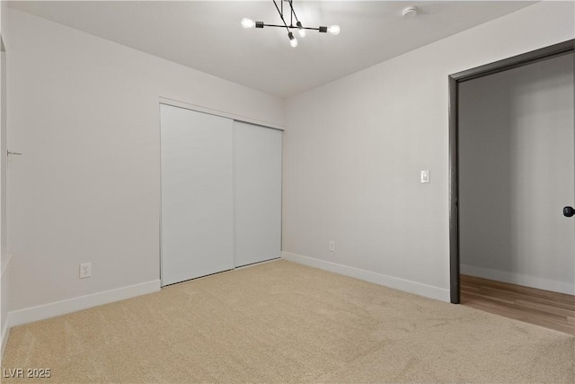 unfurnished bedroom featuring carpet floors, baseboards, a chandelier, and a closet