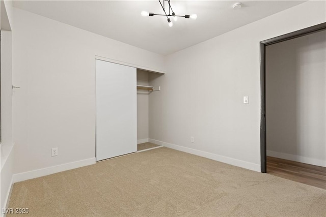 unfurnished bedroom with an inviting chandelier, baseboards, a closet, and carpet flooring