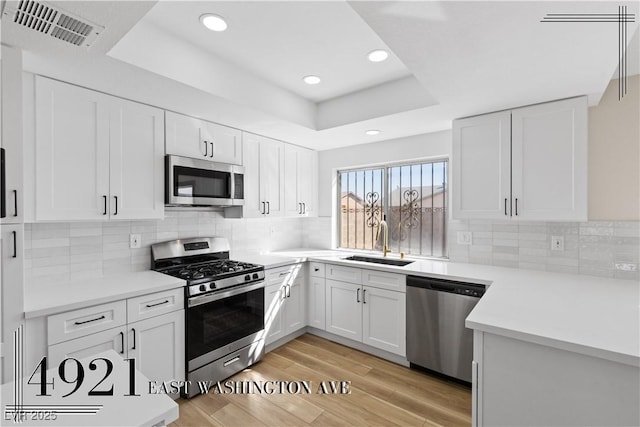 kitchen with stainless steel appliances, a raised ceiling, visible vents, light wood-style flooring, and a sink