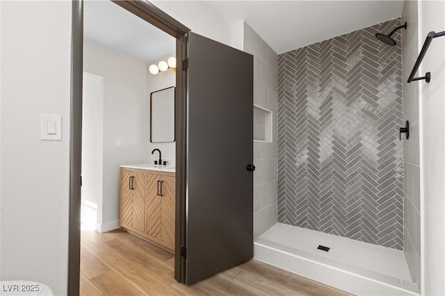 full bath with tiled shower, vanity, and wood finished floors