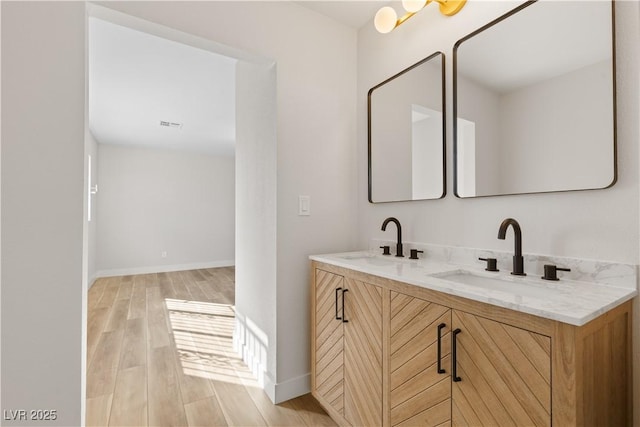 full bath featuring double vanity, wood finished floors, a sink, and baseboards