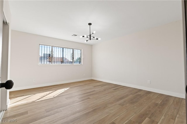 spare room featuring light wood-type flooring, visible vents, a notable chandelier, and baseboards