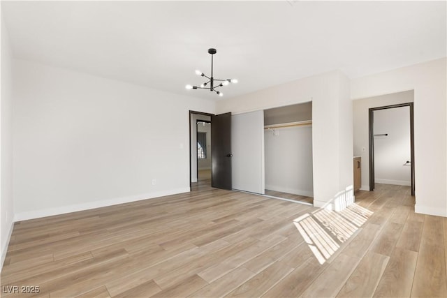 unfurnished bedroom with a chandelier, a closet, light wood-style flooring, and baseboards