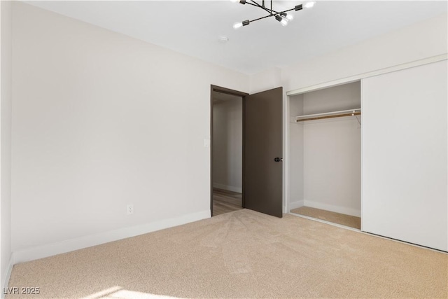 unfurnished bedroom featuring a notable chandelier, a closet, carpet, and baseboards