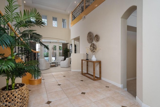 corridor featuring arched walkways, visible vents, a towering ceiling, baseboards, and tile patterned floors