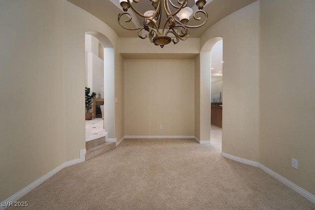 unfurnished room featuring light carpet, arched walkways, and baseboards