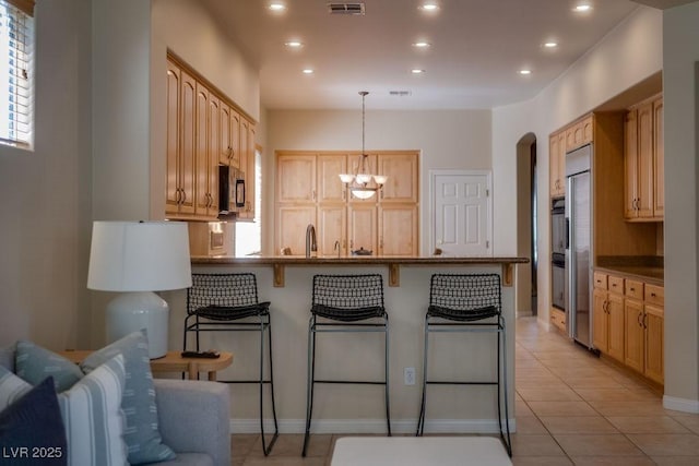 kitchen with light tile patterned floors, a breakfast bar area, a peninsula, light brown cabinetry, and recessed lighting