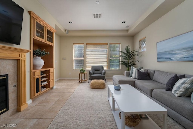 living area with light tile patterned floors, a fireplace, visible vents, baseboards, and a raised ceiling