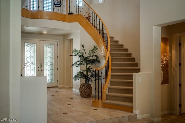 tiled entrance foyer featuring french doors, stairway, a towering ceiling, and baseboards