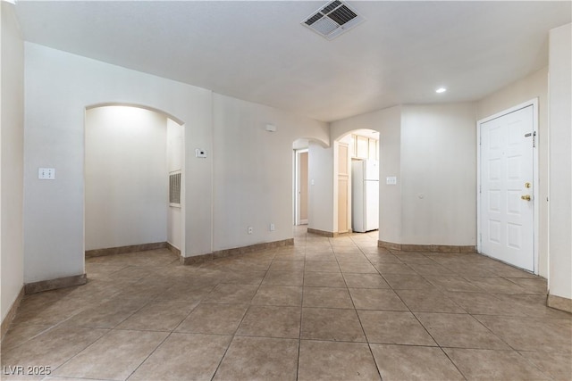 empty room with arched walkways, tile patterned flooring, visible vents, and baseboards