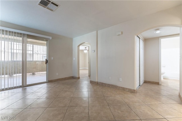 spare room featuring light tile patterned floors, visible vents, arched walkways, and baseboards