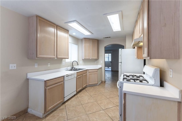 kitchen with arched walkways, under cabinet range hood, white appliances, a sink, and light brown cabinetry