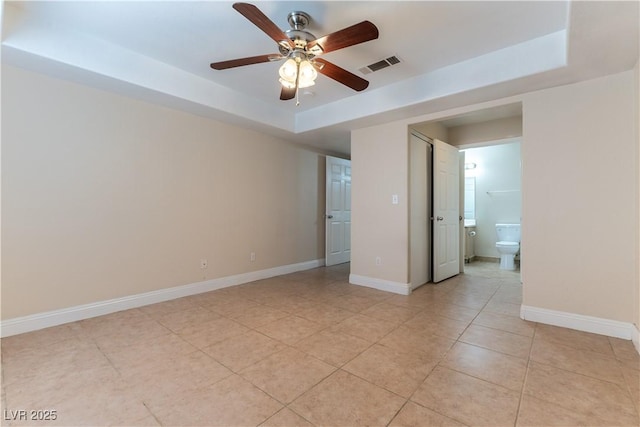 empty room with a tray ceiling, visible vents, baseboards, and light tile patterned floors