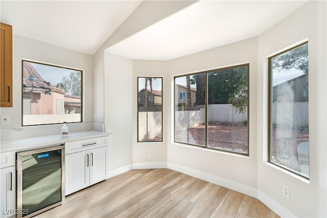 bar with light wood-type flooring, wine cooler, baseboards, and vaulted ceiling