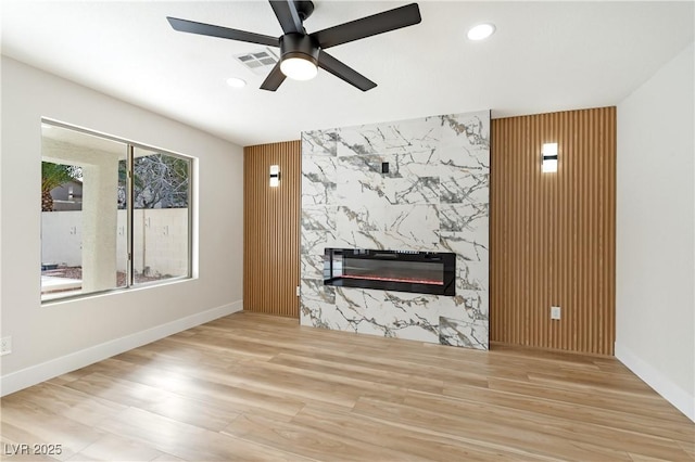 unfurnished living room with recessed lighting, an accent wall, a premium fireplace, wood finished floors, and a ceiling fan